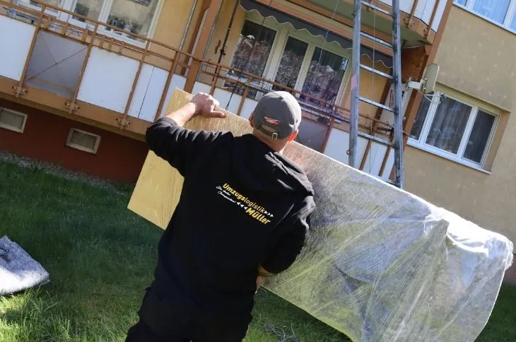 umzugshelfer traegt eingewickeltes moebelstueck vor wohngebaeude